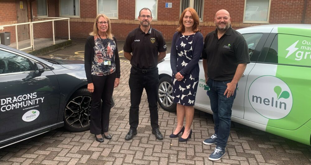 Melin Homes and Dragons RFC staff stood together in front of branded cars