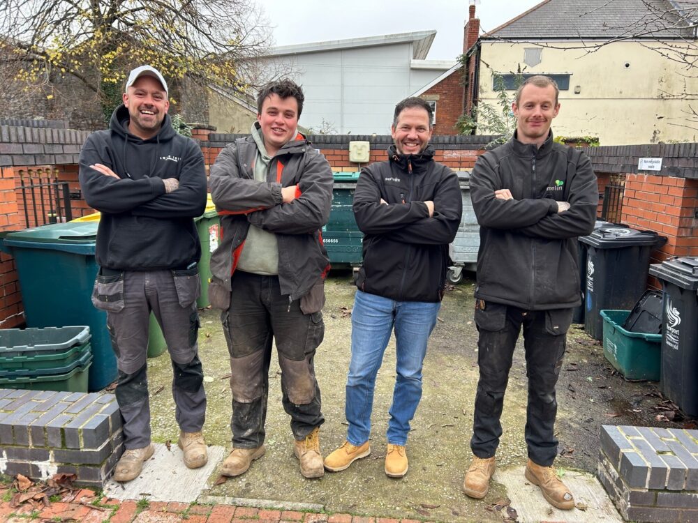 Four maintenance workers stood in front of a bin store