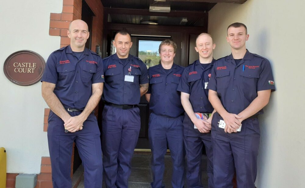 A group of firemen standing outside a block of apartments