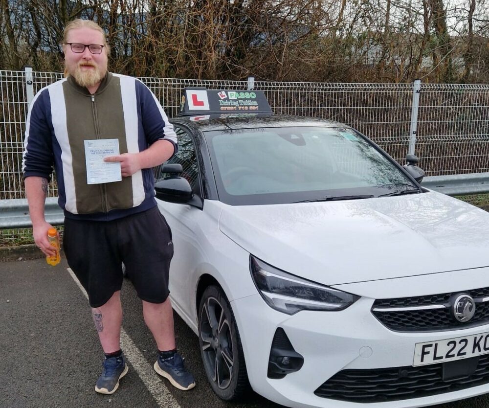 A young man stood in front of a car holding a driving test certificate