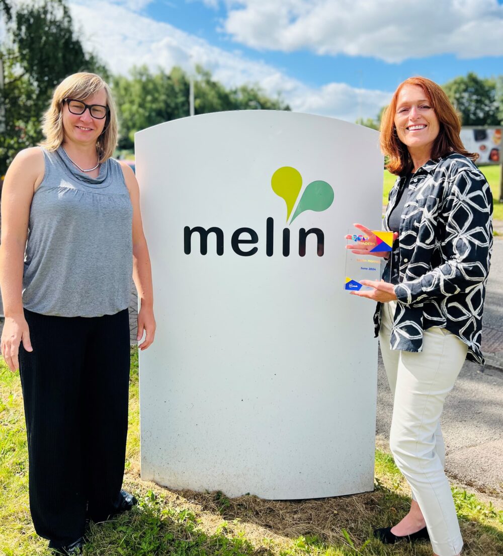Alicja Zalesinska and Melin CEO Paula Kennedy standing by a Melin sign as Paula holds the award