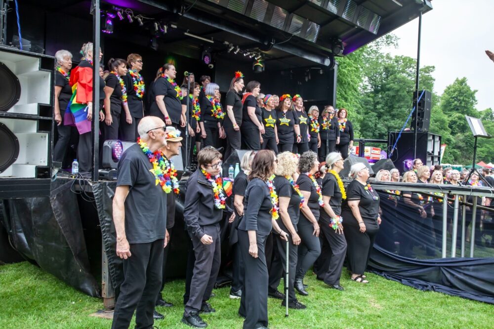 A choir performing outside on a stage wearing rainbow decorations