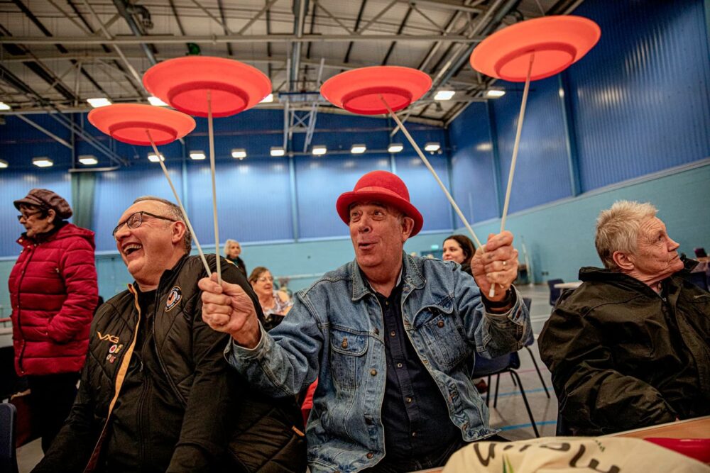 A laughing man holding four spinning plates on sticks
