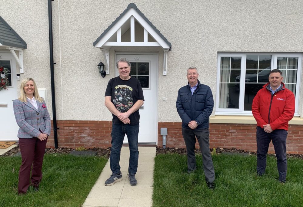 Four people stood in front of a new house, Tara Lane, BGCBC; Peter Hughes, local resident; Phil Parfitt, Melin Homebuy and Paul Phillips, Lovell.