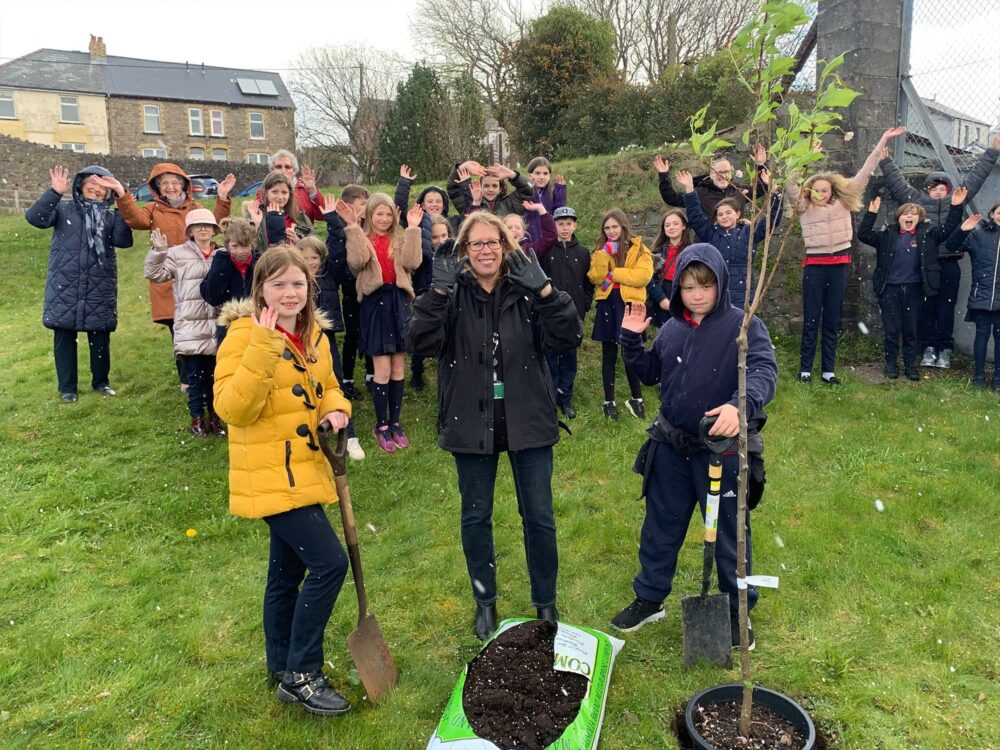 Communities Team Officer Helen Seymour planst a tree with two children while other children cheer in the background