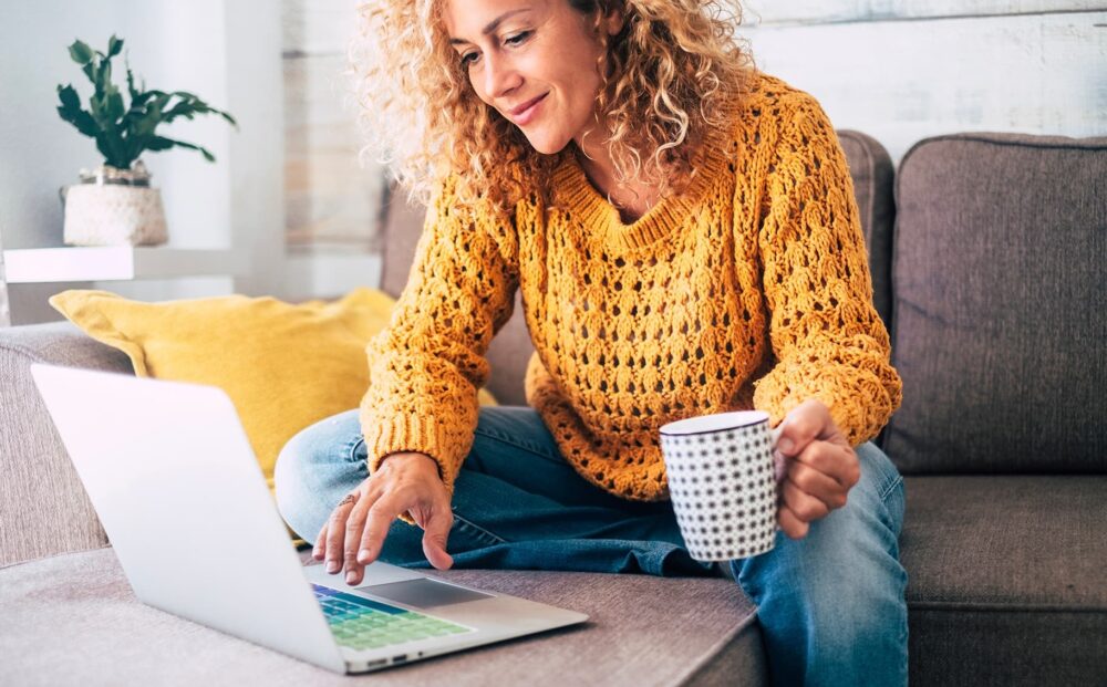 A woman at home checking her laptop with a hot drink in her hand